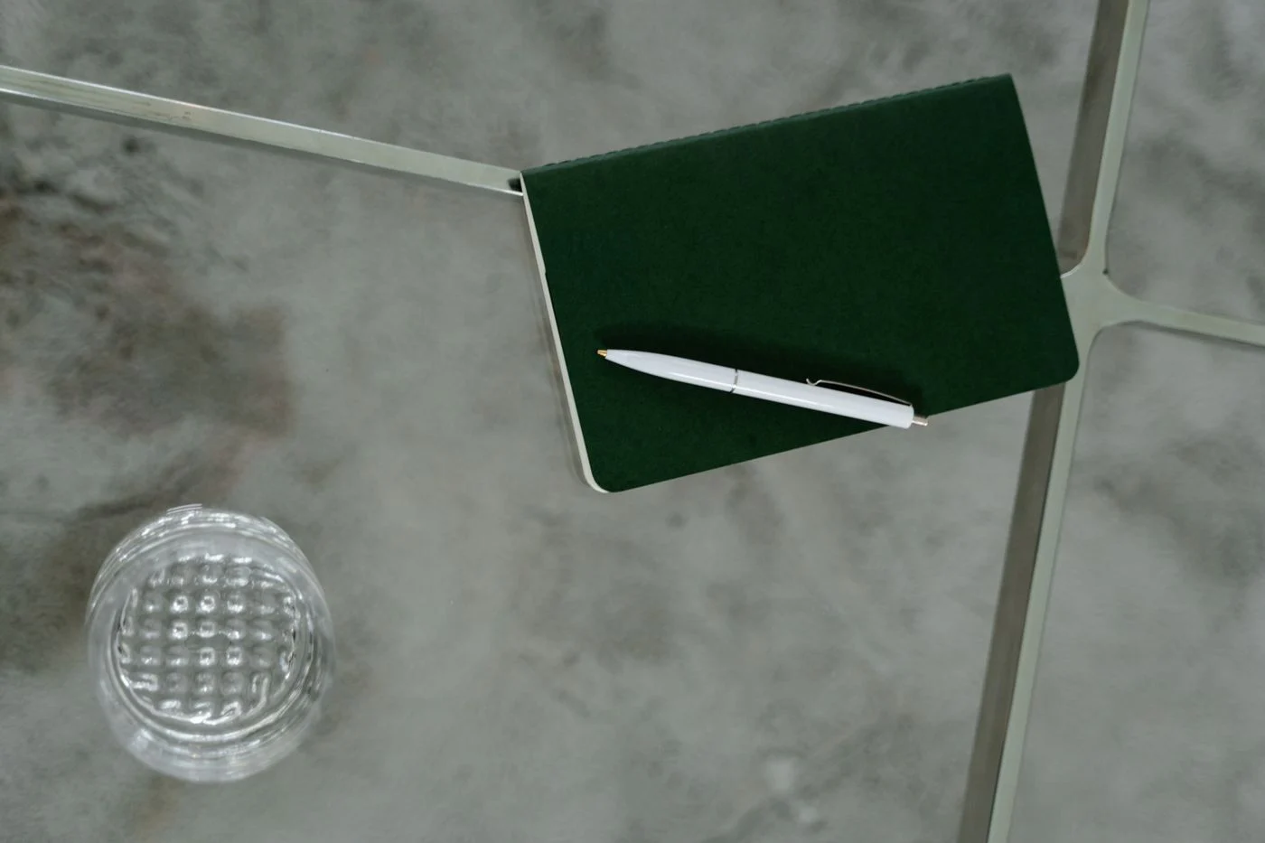 A white pen on a dark green notebook on a glass table.