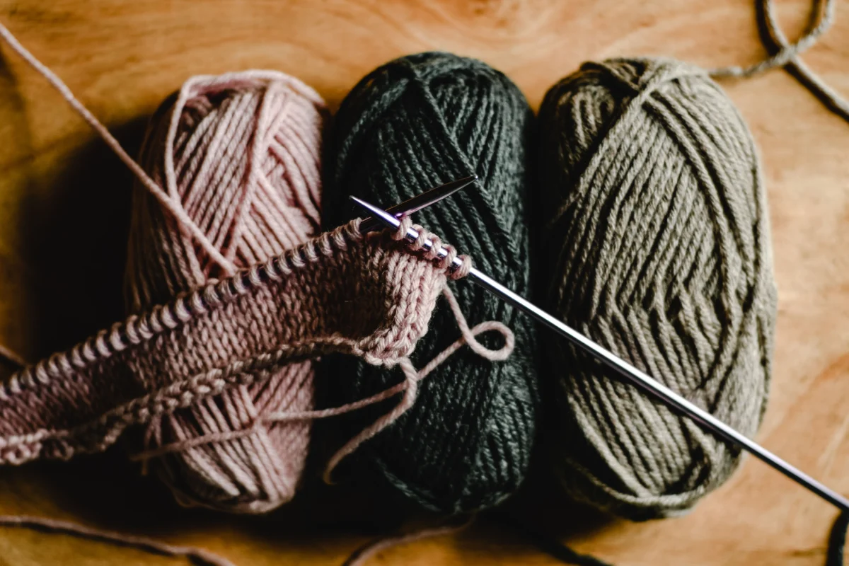 Three balls of yarn and a knitted swatch on knitting needles.