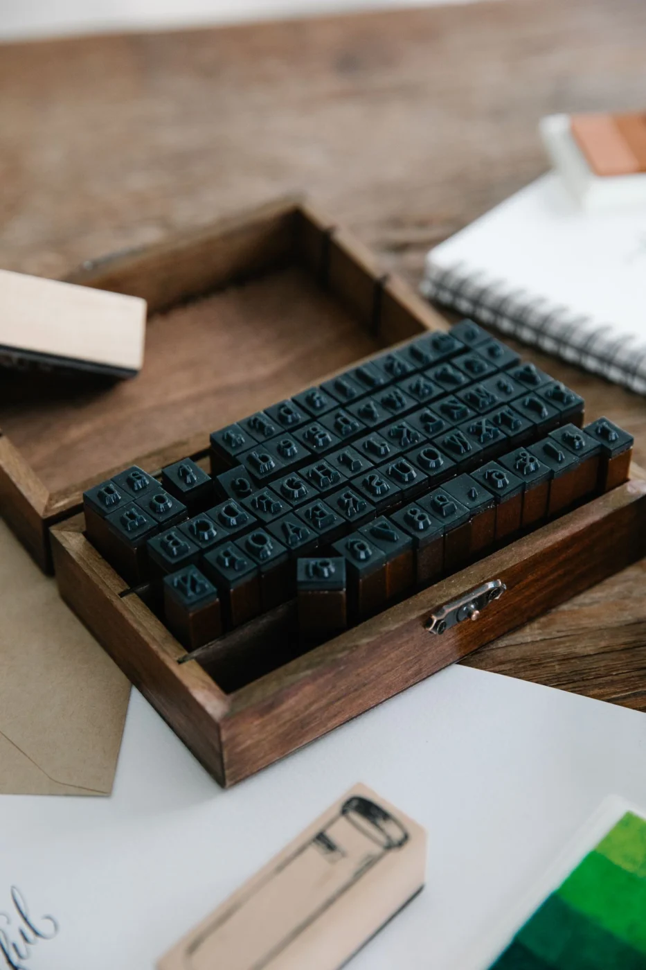 Letterpress stamps arranged in a small wooden box beside a notebook.