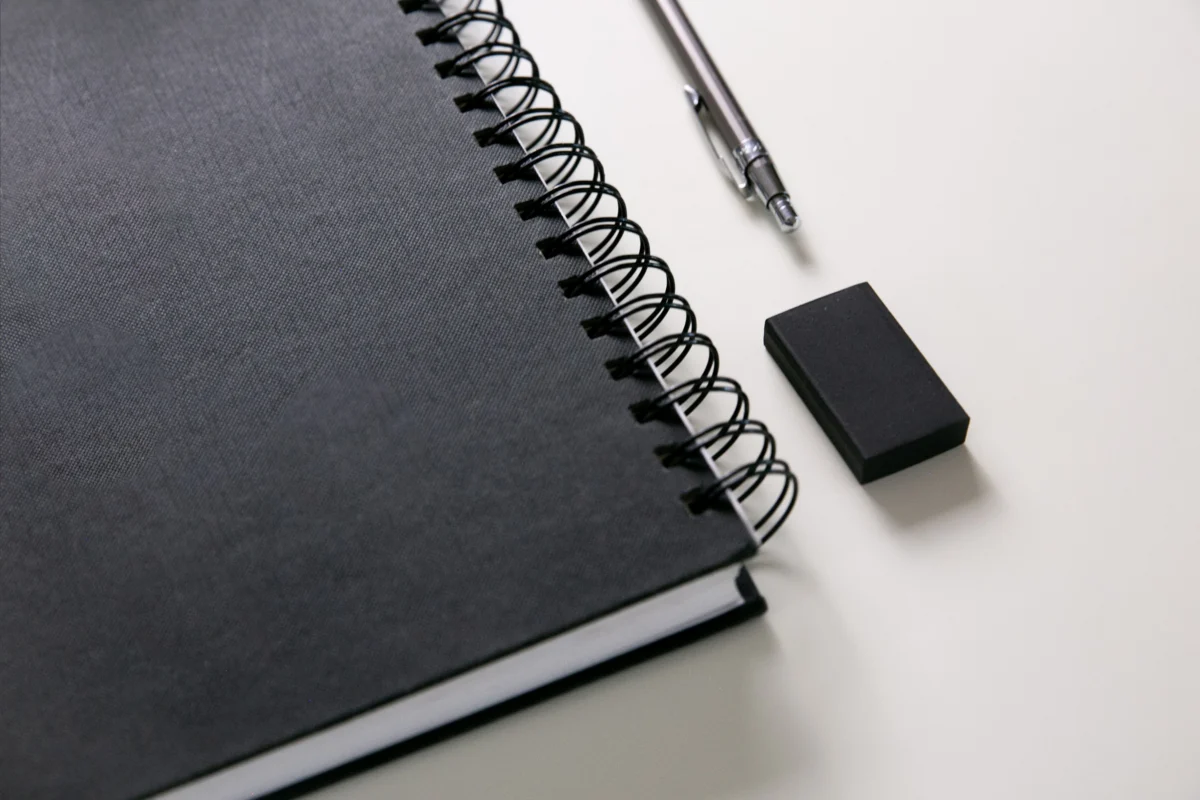 A black spiral notebook beside a pen and eraser.